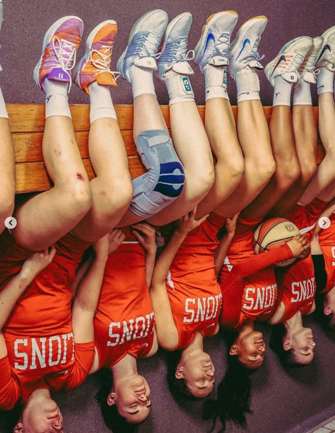 Women basketball players arranged upside down along a bench